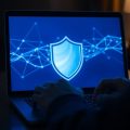 Mâini tastând la laptop, ecran cu scut de securitate.